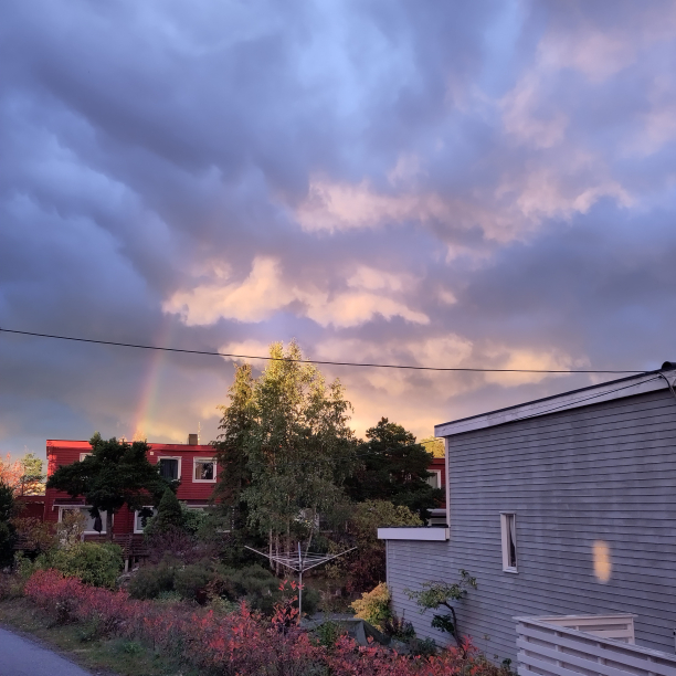 A quiet neighborhood with a rainbow and the sun setting in the background.