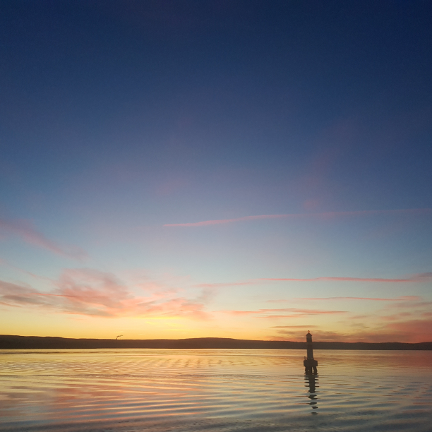 A yellow and orange sunrise on the fjord with a small lighthouse in the distance.