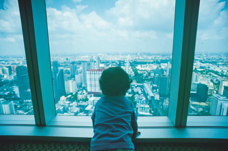 A child looking out the window of a skyscraper on the cityscape below.