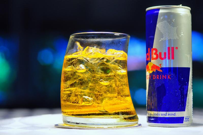 A glass of Red Bull with the can standing to the right.
