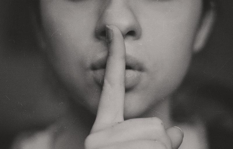 A woman holding one finger in front of her mouth in a ssshhh-fashion.