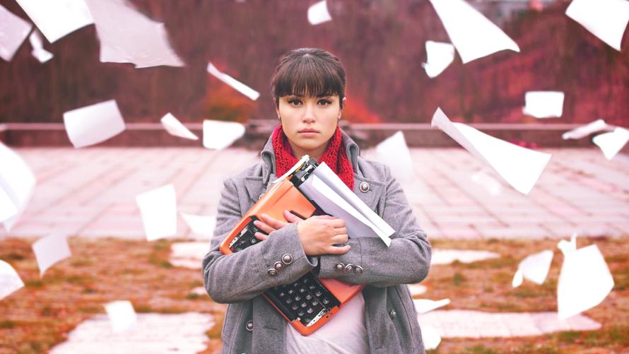 If you're suddenly able to throw papers around through sheer will, and get the thousand mile stare, it's probably a good idea to take a break. A woman with a cold, dead stare clutching a typewriter to her chest. Blank pieces of paper are falling from the sky around her.
