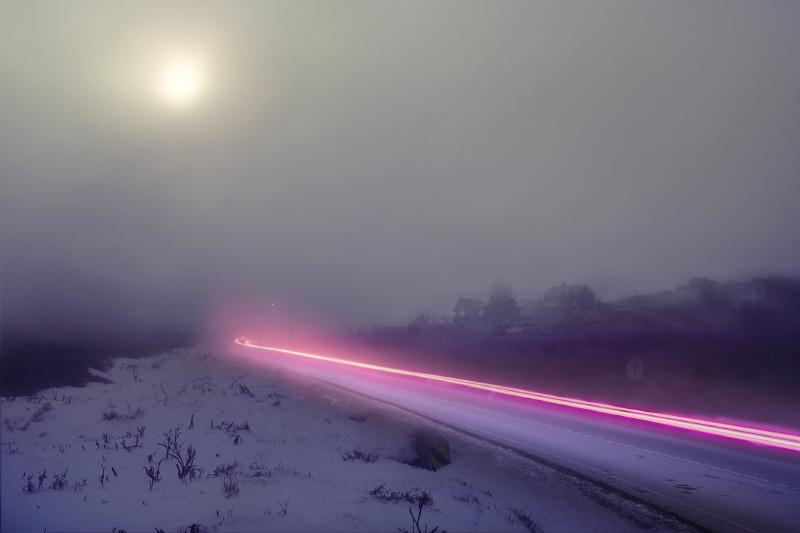 Long expsure of a foggy landscape and a road. A car has passed, the taillights exposed on the photograph.