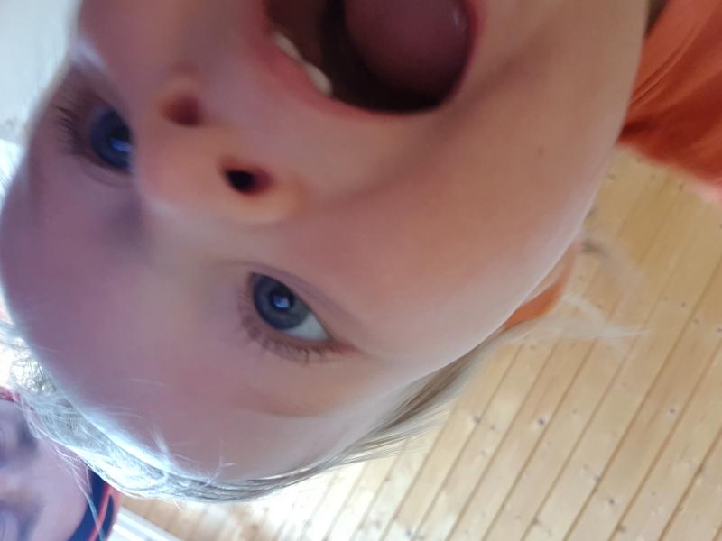 A toddler taking a selfie, looking very excited! She is half in-frame, and the picture is upside down.